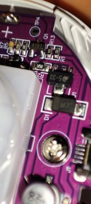 Close-up of an electronic device's circuit board with purple laminate, visible SMD components, and a mounting screw.