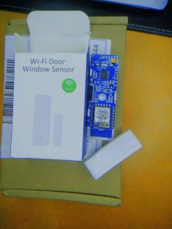 Open sensor showing electronic board next to a box labeled Wi-Fi Door Window Sensor.