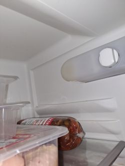 Wnętrze lodówki z osłoniętą żarówką i produktami spożywczymi na półce.