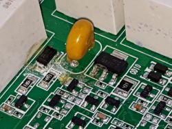 Zbliżenie na płytkę drukowaną z widoczną korozją wokół komponentów elektronicznych.