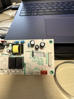 Electronic board with a laptop charger in the background.