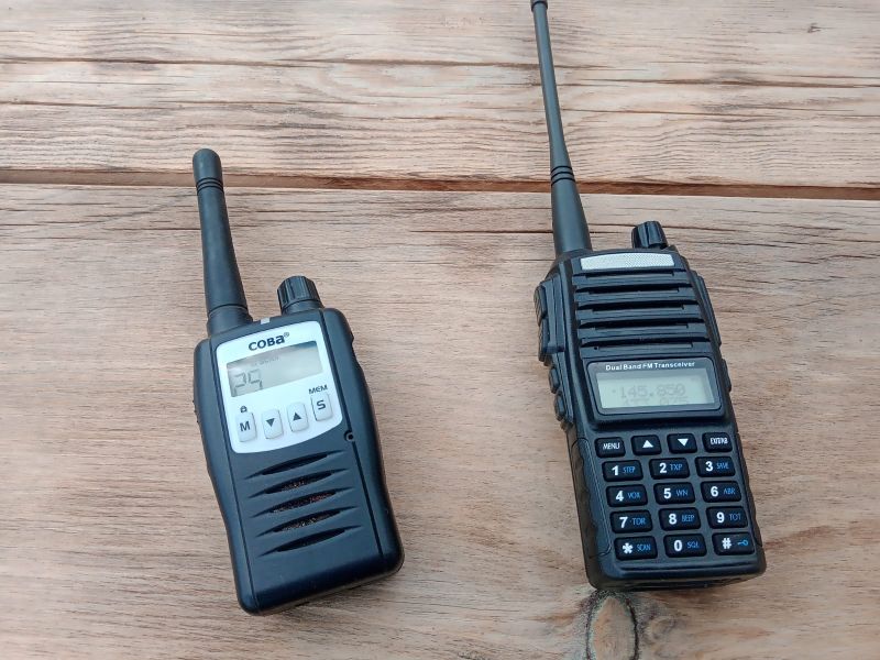 Dwa radiotelefony na drewnianym stole: COBRA i Baofeng UV-82 z wysuniętymi antenami