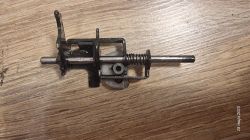 Element mechanizmu wiertarki leżący na drewnianym blacie, z widoczną sprężyną i metalowymi częściami.