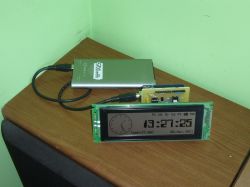 LCD display with a clock connected to a powerbank on a table.
