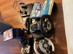 Zestaw akcesoriów do konsoli PlayStation 2, w tym kierownice z pedałami, pady, gry i karty pamięci.