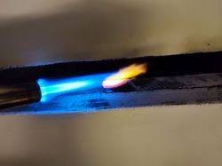 Blowtorch heating a metal plate, causing it to glow.