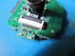 Camera Module with PCB Electronic module with camera lens and flat cable connector on a blue background.