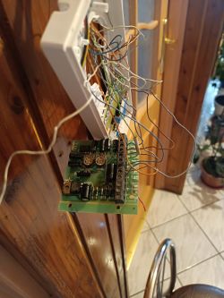 Widok z bliska na otwarty domofon z widoczną wewnętrzną płytką elektroniczną i podłączonymi przewodami.