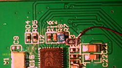Close-up of a green printed circuit board with SMD electronic components, traces, and a soldered red wire.