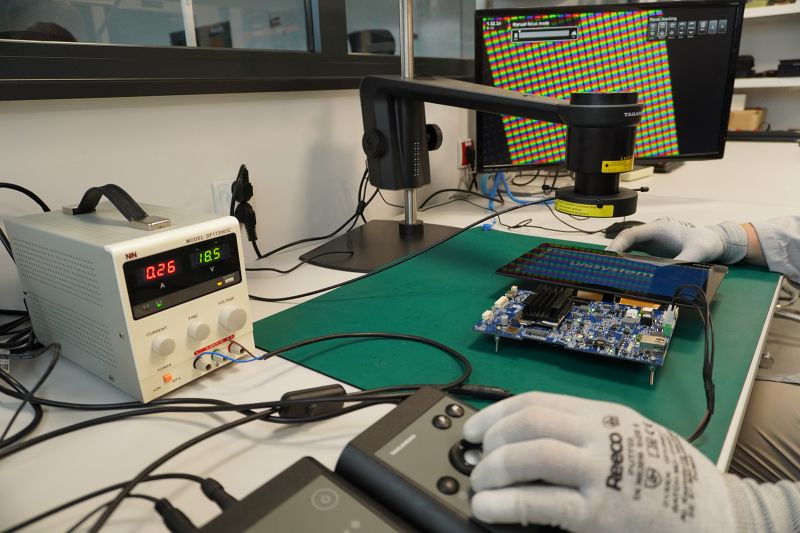 Gloved person testing a display and PCB board in a laboratory setup.