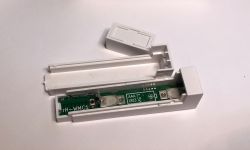 Rozebrany biały plastikowy czujnik z widoczną płytką elektroniczną i miejscem na baterię AAA.