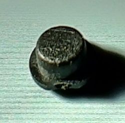 Kleines schwarzes zylindrisches Kunststoffteil auf hellem, gebürstet wirkendem Hintergrund