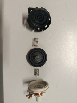 Rozłożony mechaniczny presostat z widocznymi sprężynami i membraną na białym tle