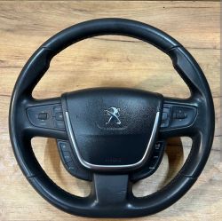 Czarna kierownica Peugeot z przyciskami sterowania po bokach, widok z góry na drewnianym tle