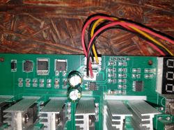 Fragment zielonej płytki PCB z radiatorami, kondensatorami i przewodami w złączach; po prawej wyświetlacz LED.
