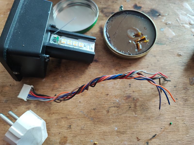 Disassembled Electronic Device with LEDs and Wires Opened electronic device with visible LED lights and wires on a wooden surface.