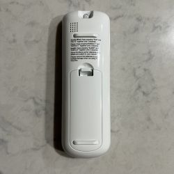 Back of a white remote control lying on a light countertop.
