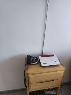 Router Fritz!Box i telefon stacjonarny na drewnianej szafce przy ścianie