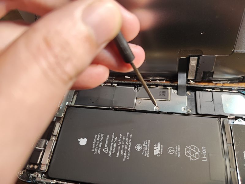 iPhone Battery Replacement — Disassembly Step Person unscrewing screws inside an open iPhone.