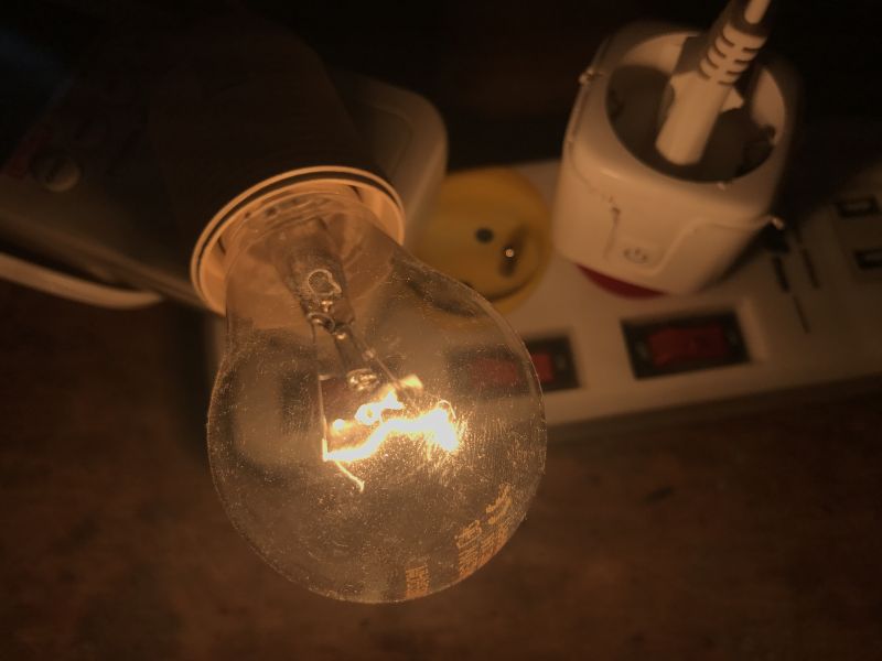Lit Light Bulb Connected to Power Strip Close-up of a lit light bulb connected to a power strip with other electronic devices.