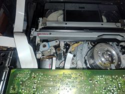 Wnętrze magnetowidu VHS z włożoną kasetą, widoczne mechanizmy i płytka drukowana