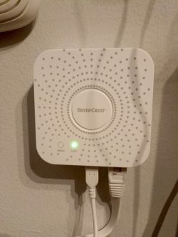 White SilverCrest Zigbee gateway on a wall with Ethernet cable and power lead connected