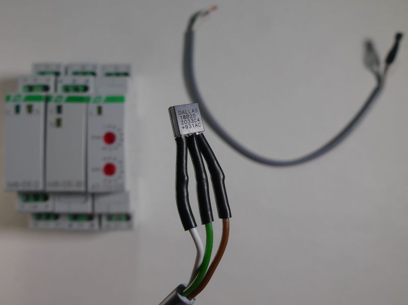 Czujnik temperatury Dallas DS18B20 podłączony do przewodów, na tle szafy elektrycznej.