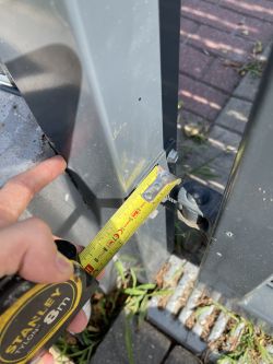 Pomiar szerokości między słupkiem a ramą furtki miarką taśmową.