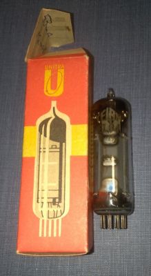 Lampa elektronowa EL84 stojąca obok oryginalnego pudełka Unitra na niebieskim tle.