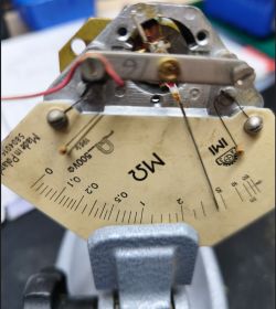 Zbliżenie na mechanizm i tarczę analogowego miernika z napisem „MΩ” i logo IMI