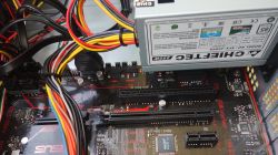 Fragment wnętrza komputera z widocznym zasilaczem Chieftec 250W oraz płytą główną ASUS z wolnymi slotami PCIe.