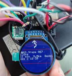 Okrągły wyświetlacz z ikoną skrętu, otoczony przewodami i modułami elektroniki