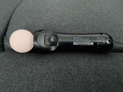 Kontroler Sony PlayStation Move leżący na szarej tkaninie, widoczny przycisk T.