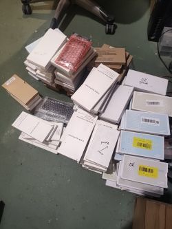 Stosy opakowań z oznaczeniami LCD i ekranami dotykowymi leżące na podłodze obok krzesła biurowego