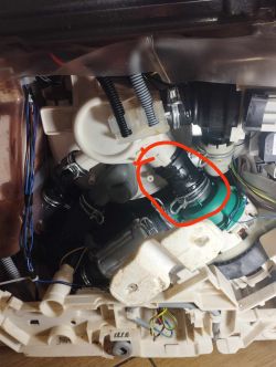 Fragment wewnętrznego mechanizmu urządzenia, z zaznaczonym wężem podłączonym do białego elementu.
