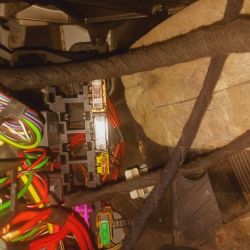 Skrzynka bezpieczników w samochodzie z widocznymi kolorowymi kablami.