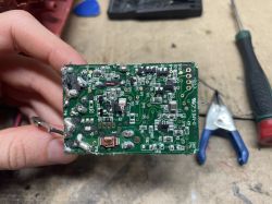 Dłoń trzyma zieloną płytkę PCB z elementami SMD i śladami lutowania na stole warsztatowym