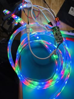 The image shows an RGB LED strip and a controller placed on a wooden table.