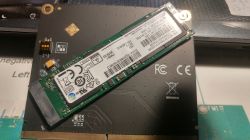 Zbliżenie na adapter z zamontowanym dyskiem NVMe i trzema małymi przełącznikami.