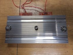 Radiator aluminiowy z przymocowanymi matami grzewczymi i przewodami na drewnianej powierzchni