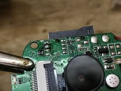 Close-up of a webcam's PCB with visible electronic components and a soldering clamp.