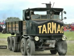 Czarny parowy samochód ciężarowy z napisem „TARMAC”, stojący na trawie, z parą przy kołach.