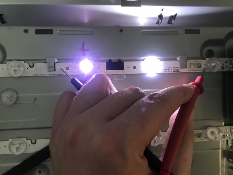 Testing LED Lights in a TV A hand holding wires connected to an LED tester examining TV backlighting.