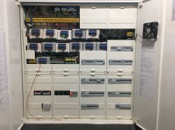 An electrical box filled with electronic devices and controllers, with a mounted fan.
