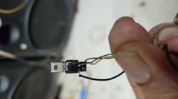 Close-up of a damaged micro-USB plug with exposed wires held between fingers