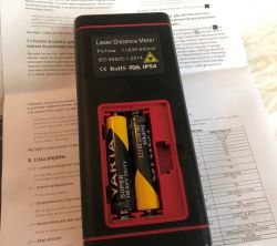 Dalmierz laserowy Lertz LZTS80 z odsłoniętą komorą baterii i dokumentacją w tle.