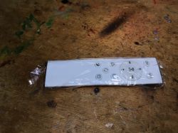 Plastic-wrapped white remote with several buttons on a wooden surface.