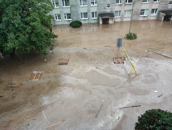 Zalane podwórko z wodą sięgającą niemal do drzwi budynku mieszkalnego.