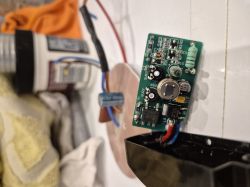 Płytka elektroniczna wyjęta z obudowy zbliżona do aparatu, w tle kabel i pojemnik.