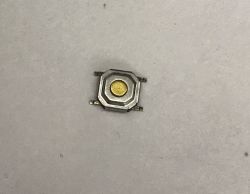 Small metal electronic push button with four leads on a light background.